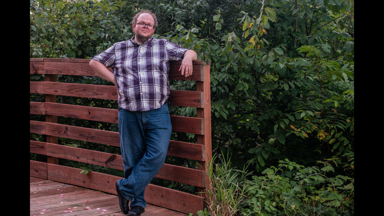Alex standing on bridge with legs crossed.