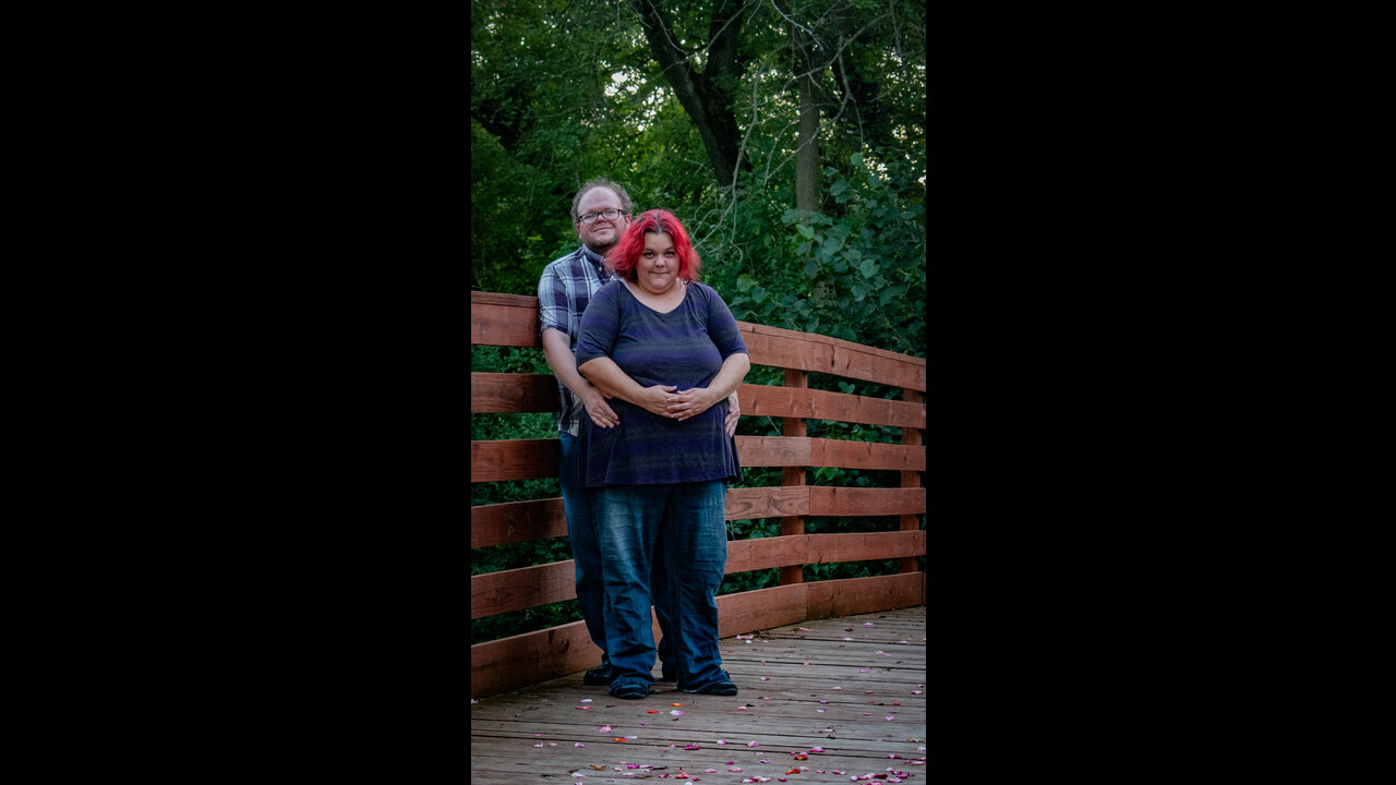 Alex standing with arms around Danni at side of bridge.