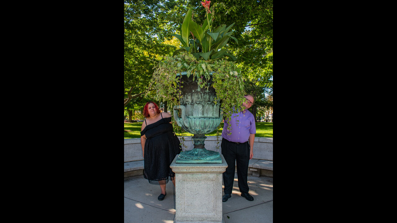 Danni and Alex peeking out from behind very large flower pot at Wisconsin State Capitol.